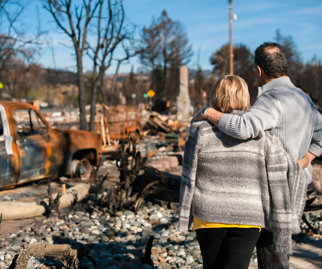 A man and woman standing in a burnt-down area, observing the destruction left by fire